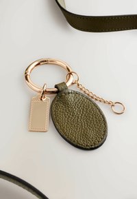 Oliivroheline nahast võtmehoidja tekstureeritud ovaalse sildiga ja kuldse rõngaga, mille küljes on keti abil kinnitatud kuldsega aktsendiga ristkülikukujuline silt.