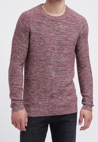 Rood en grijs gemêleerd gebreid sweater met een ronde hals en lange mouwen, voorzien van geribde manchetten en zoom, gecombineerd met donkere jeans.