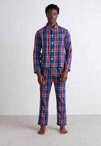 Conjunto de pijama de algodón a cuadros azules y rojos que incluye una camisa con botones y cuello, y pantalones a juego, mostrado en un modelo descalzo.