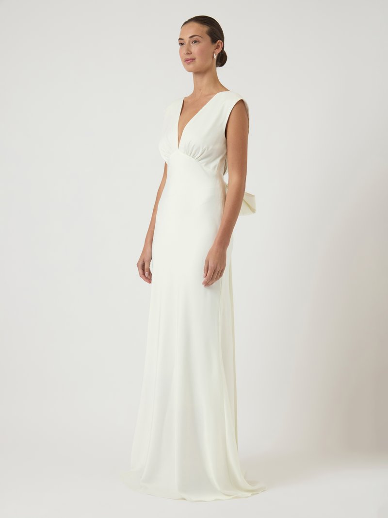 Λευκό, αμάνικο φόρεμα με βαθύ ντεκολτέ και σφηκοειδές στη μέση. Διαθέτει απαλό, ρέον ύφασμα και φιόγκο στο πίσω μέρος.