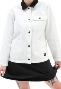 Veste en denim blanche avec un col en velours côtelé noir, des boutons noirs, deux poches avant et une étiquette de marque noire sur l'ourlet.