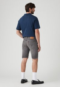 Laivaston värinen polo-paita, harmaat farkkushortsit, valkoiset sukat ja mustat loafers-kengät. Shortseissa on nahkaremmi ja haalistunut pesu näkyvine ompeleineen.