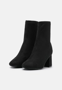 Bottines en daim noir avec une texture lisse, un bout pointu et un talon épais. Présentent une couture minimale et un design sans coutures.