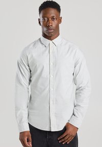 Camisa de botones rayada en gris claro y blanco, con mangas largas, cuello estándar y cierre frontal de botones, hecha de una tela suave.