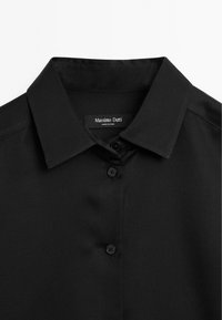 Svart skjorta med knappar, klassisk krage, slät textur och tre knappar fram. Etikett med texten "Massimo Dutti."