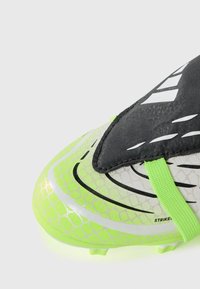 Fotballsko med et gjennomsiktig nett design som har grønn og svart fargekombinasjon, teksturert overflate og et fremtredende belte over toppen.
