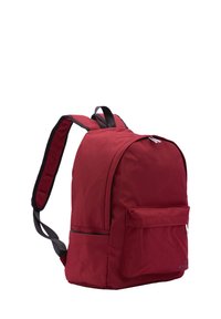 Sac à dos en tissu rouge de forme arrondie, comportant des bretelles noires réglables, une poche avant et une fermeture éclair sur le dessus.