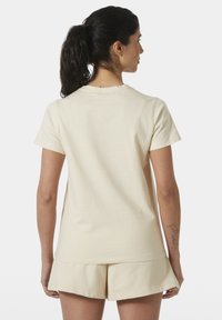 Beige bavlněné tričko s krátkým rukávem, kulatým výstřihem a volným střihem. Nosí se s jemně barevnými béžovými šortkami. Žádné viditelné vzory ani detaily.