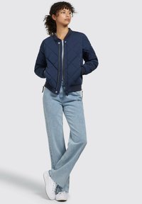 Chaqueta bomber acolchada en color navy con cuello redondo, cierre frontal y bolsillos laterales, combinada con jeans de lavado claro y zapatillas blancas.