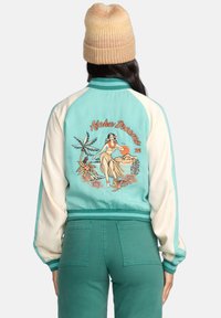 Teal and cream color-blocked jacket with a floral and hula dancer embroidered design on the back. Ribbed cuffs and waistband.