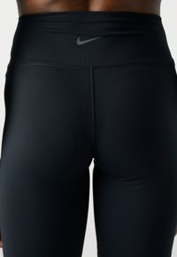 Czarne legginsy sportowe wykonane z elastycznego, gładkiego materiału, z wysokim stanem i małym szarym logo Nike na środku pleców.
