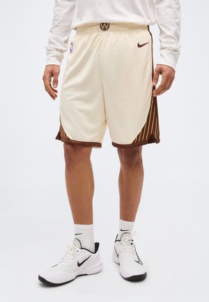 Mann trägt cremefarbene NBA-Basketballshorts mit braunen und gelben gestreiften Seitenpanelen, weiße Nike-Socken und weiße Nike-Sneaker.