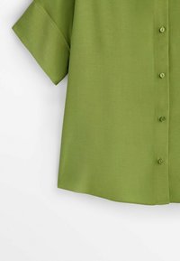Chemise verte à manches courtes en tissu lisse, dotée d'une patte de boutonnage et d'une coupe décontractée. La couleur est uniforme sans motifs.