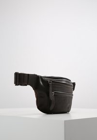 Braune Leder-Umhängetasche mit strukturiertem Finish, ausgestattet mit mehreren Reißverschlussfächern und einem verstellbaren Riemen. Kompaktes und funktionales Design.