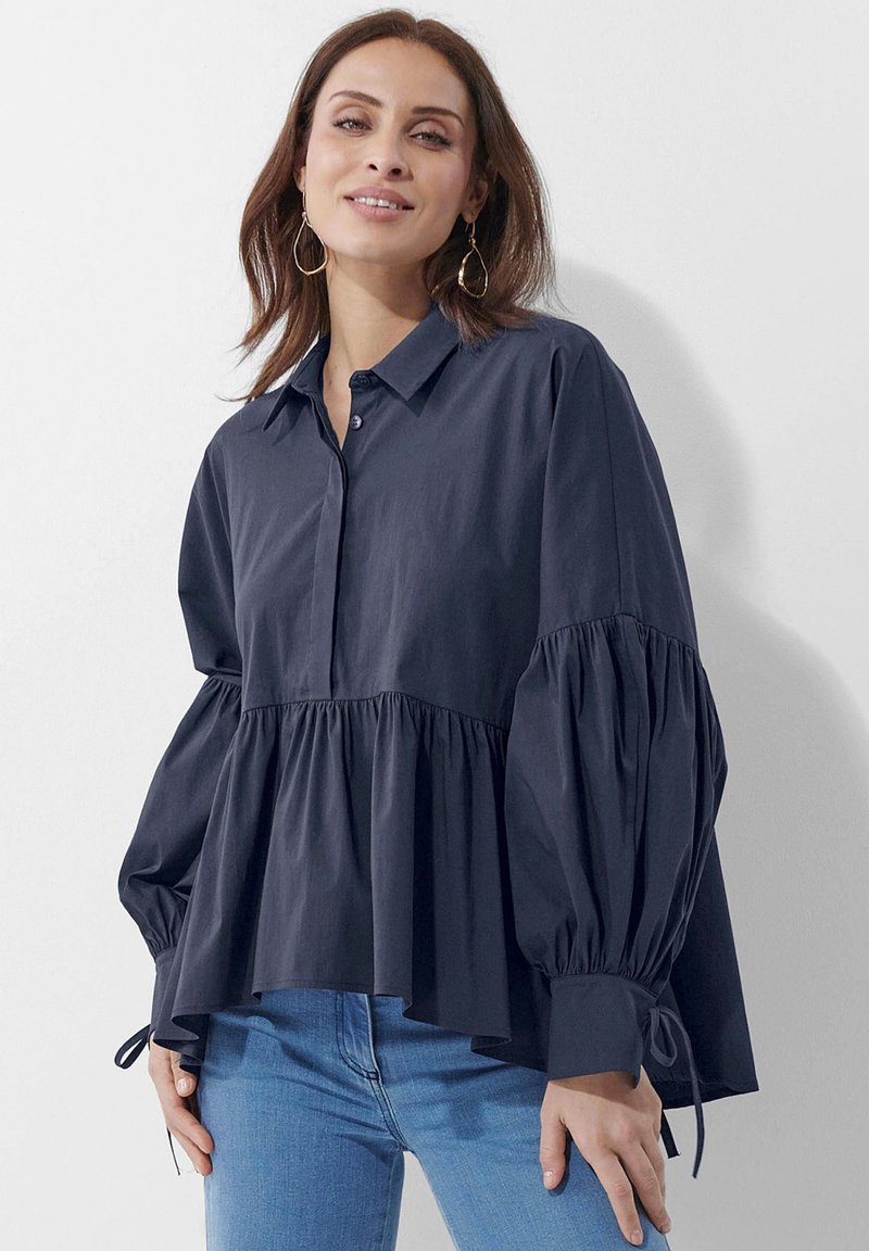 Marineblaue Baumwollbluse mit einem Kragen zum Knöpfen, gepufften Ärmeln und einem gestuften Rüschendesign. Mit Bändern an den Ärmelsäume akzentuiert.