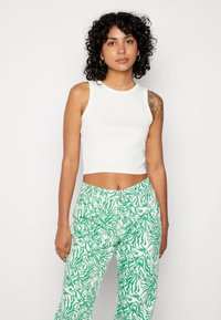 Camisola de alças branca com bainhas, combinada com calças largas verdes e brancas com um padrão ondulado e um corte descontraído.