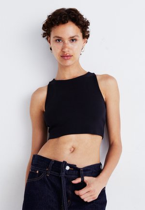 Top corto negro de canalé con un cuello alto y diseño sin mangas. Combinado con unos jeans oscuros de mezclilla de tiro alto que presentan un cinturón.