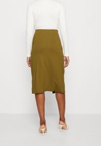 Oliivinvihreä hame, pehmeästä kankaasta, polvenmittainen malli, jossa hillitty sivuhalkio, yhdistettynä beigenvärisiin korkeakorkoisiin sandaaleihin.