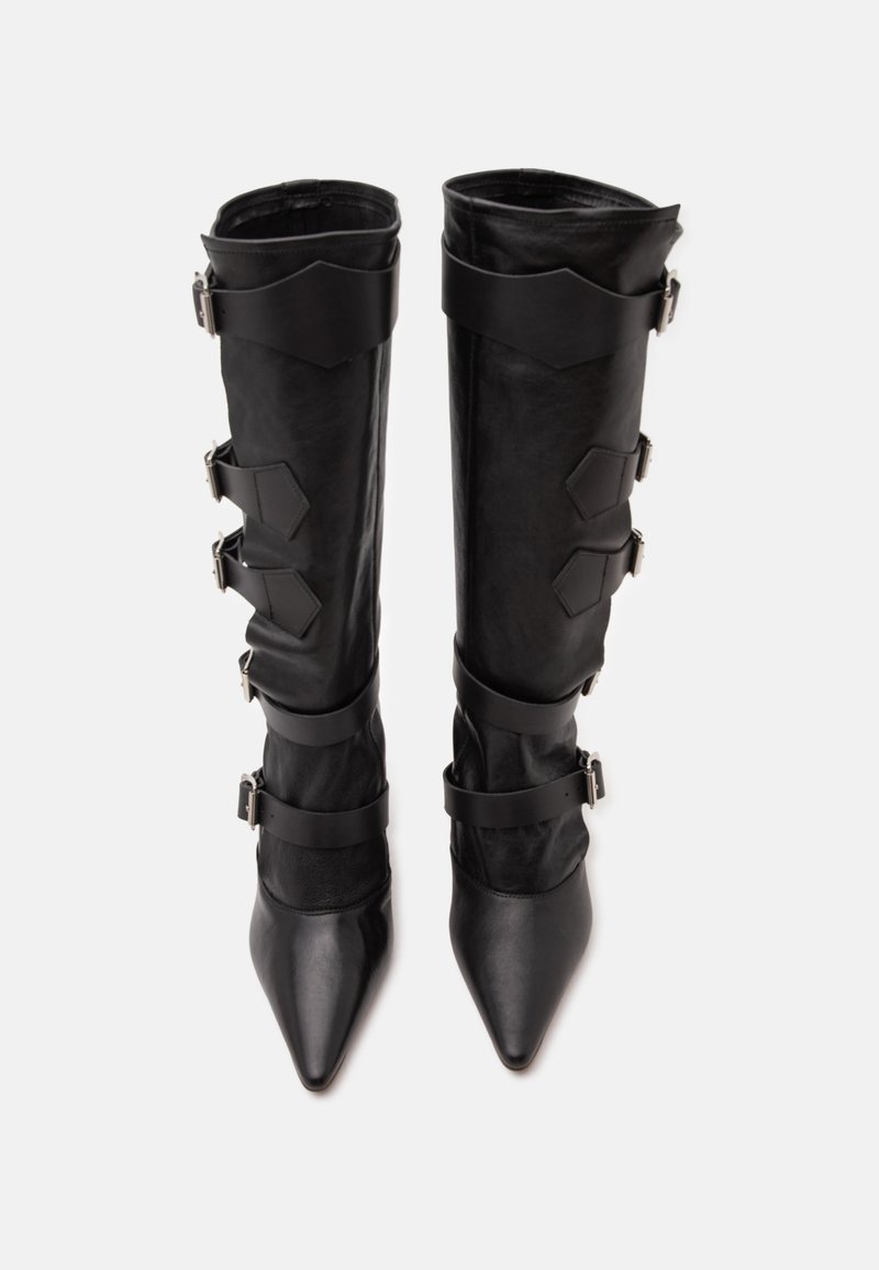 Pair of tall black leather boots with pointed toes and multiple adjustable straps with silver buckles on a white background.