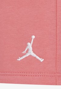 Svijetloružičasta tkanina s bijelim izvezenim Jumpman logom. Dizajn je jednostavan s finim šavovima i glatkom teksturom.