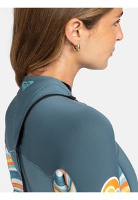 Neoprenový oblek s designem na půl zip, v modro-šedém materiálu s v�ícebarevnými pruhovanými vzory na boku, hladkou texturou a detailním logem.