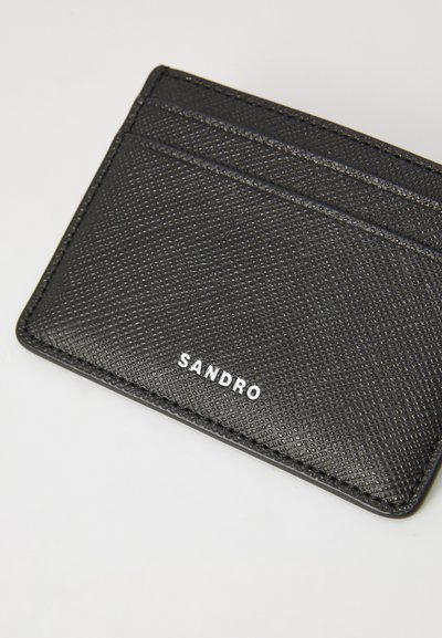 Black textured cardholder featuring four card slots, embossed logo "SANDRO" in white, and slim, rectangular design. Durable material.