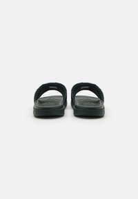 Sandales en caoutchouc noires avec un dos ouvert et deux larges sangles, semelle intérieure texturée et semelle lisse. Design minimaliste sans accents supplémentaires.