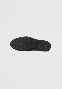 Schwarze Schuhsohle mit einem strukturierten Muster, das geometrische Formen und Rillen für besseren Halt aufweist. Größe angegeben als 37.