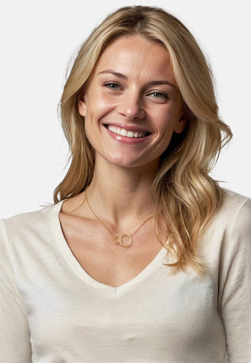 Guldhalskæde med to sammenflettede cirkler, båret over en lysefarvet v-hals t-shirt. Glat metaloverflade, enkelt design med minimale udsmykninger.
