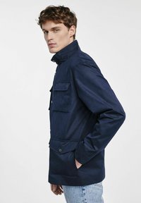 Granatowa kurtka wykonana z teksturowanej tkaniny, z wysokim kołnierzem, przednimi kieszeniami i zapięciem na napy. Casualowy styl z klasycznym krojem.