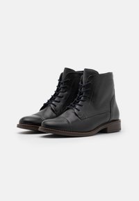 Bottines en cuir noir avec bout arrondi, lacets à l'avant et texture lisse. Semelle marron avec un petit talon, détails de couture minimaux.