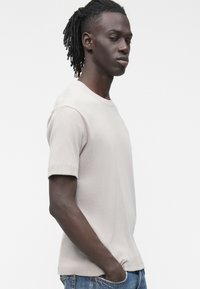 Tricou gri deschis cu mâneci scurte, textură nervurată, decolteu rotund și croială dreaptă. Purtați cu blugi din denim albastru.