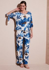 Completo floreale in due pezzi composto da una blusa ampia e pantaloni a gamba larga nei toni del blu, bianco e marrone. Tessuto testurizzato con dettagli legati.