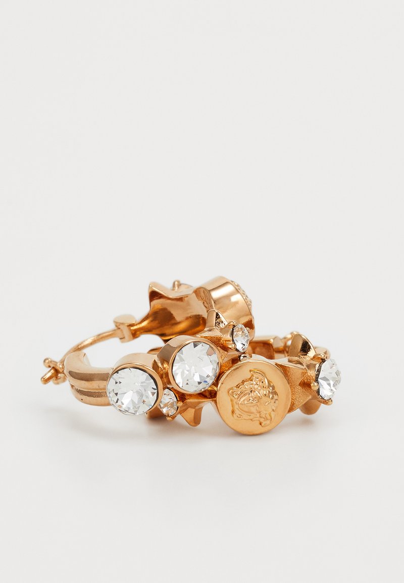 Goldfarbener metallischer Ring mit drei klaren Kristallen, texturierter Oberfläche und einem runden Anhänger mit erhabenen Designs.
