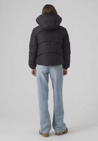 Zwarte pufferjack met een capuchon, met doorgestikte naden en een relaxte pasvorm. Gekocht met lichtblauwe flare jeans en bruine laarzen.