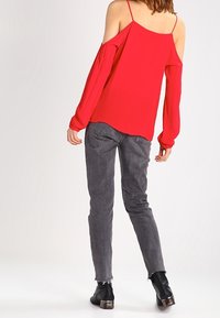 Rød kold-skulder bluse med lange ærmer, parret med grå taperede jeans. Jeansene har en frynset kant og er afsluttet med sorte ankelstøvler.