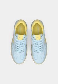 Ανοιχτό μπλε αθλητικά παπούτσια με υφή δέρματος, κίτρινες λεπτομέρειες στη γλώσσα και στο πλάι, και άσπρες κορδόνες. Διαθέτει καουτσούκ σόλα.