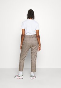 Bruna rutiga byxor med hög midja, som har en lös passform och sidofickor, kombinerat med en vit t-shirt och färgglada sneakers.