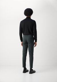 Camisola preta de mangas longas, com design justo. Calças justo de cor verde escuro com bolsos traseiros. Sapatos pretos com sola grossa.