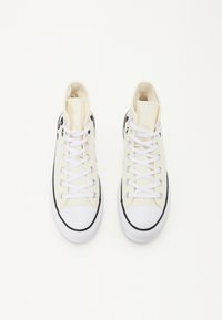 Höga sneakers i krämfärgad canvas med svarta accenter. Har vita snören, gummitåhätta och slät textur. Klassisk design.