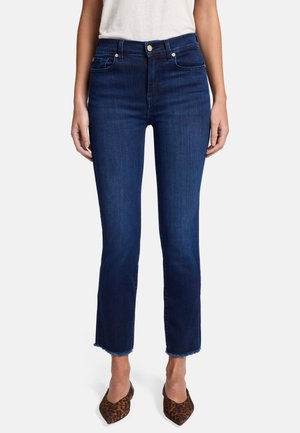 Donkerblauwe cropped denim jeans met een hoge taille, lichte stretch en rafelranddetails, gecombineerd met bruine schoenen met een luipaardprint en hak.