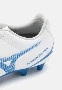 Crampons de football blancs avec des accents bleus, fabriqués en matériau synthétique lisse. Présente un col texturé et une couture visible, avec une marque sur le côté.