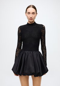 Black dress featuring a lace top with long sleeves and a mock neckline, transitioning to a satin balloon skirt with a smooth texture.