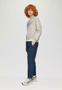 Grijze sweatshirt met een metallic graphic, gecombineerd met marineblauwe tapered broek en zilveren sneakers. Eenvoudig ontwerp, casual uitstraling, textielstof.