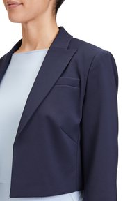 Marineblauwe cropped blazer van soepel materiaal, met een pieklapel en een enkele borstzak, gecombineerd met een lichtblauwe top eronder.