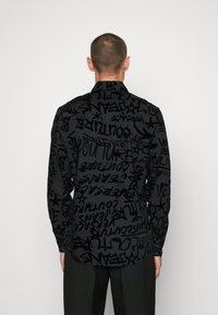 Maglietta nera con stampa a graffiti su tutta la superficie in diverse tonalità di nero. Maniche lunghe con colletto standard e orlo curvo.