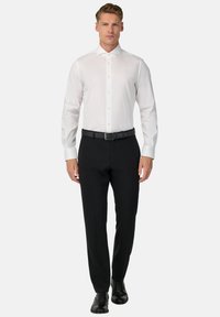 Camicia bianca a maniche lunghe con chiusura a bottoni, abbinata a pantaloni neri e una cintura nera. Scarpe in pelle nere completano l'outfit.