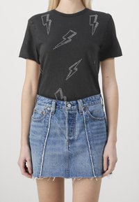 Zwarte t-shirt met zilveren bliksemflitspatronen, gecombineerd met een lichtblauwe denim rok met rafelige zoom, featuring een hoge taille en voorzakken.