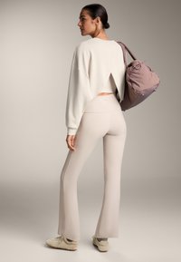 Világos bézs, rövid fazonú pulóver hátul kivágással, magas derekú, világos bézs harangnadrággal párosítva. Barna edzőcipő és egy puha lila táska.