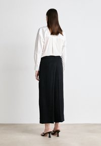 Λευκό πουκάμισο με μακριά μανίκια, μαύρο παντελόνι φάρδυ, απαλό ύφασμα, μποτάκια μέχρι τον αστράγαλο, απλός σχεδιασμός, χωρίς ορατά σ�χέδια, θεαθείς από πίσω.